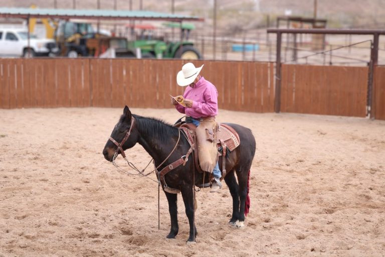 A cowboy reads a Cowboy Days Program while on horseback riding